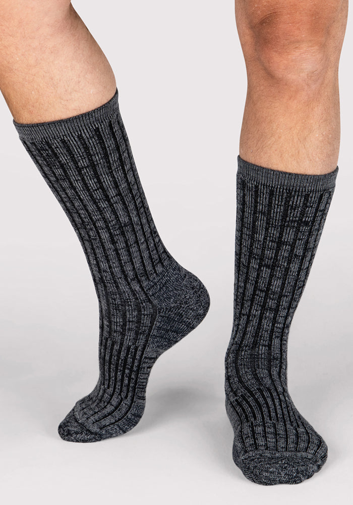 A close-up of a person wearing Woolx Mens Joey Crew Socks in Stone Grey, standing on a light background with one foot slightly raised.