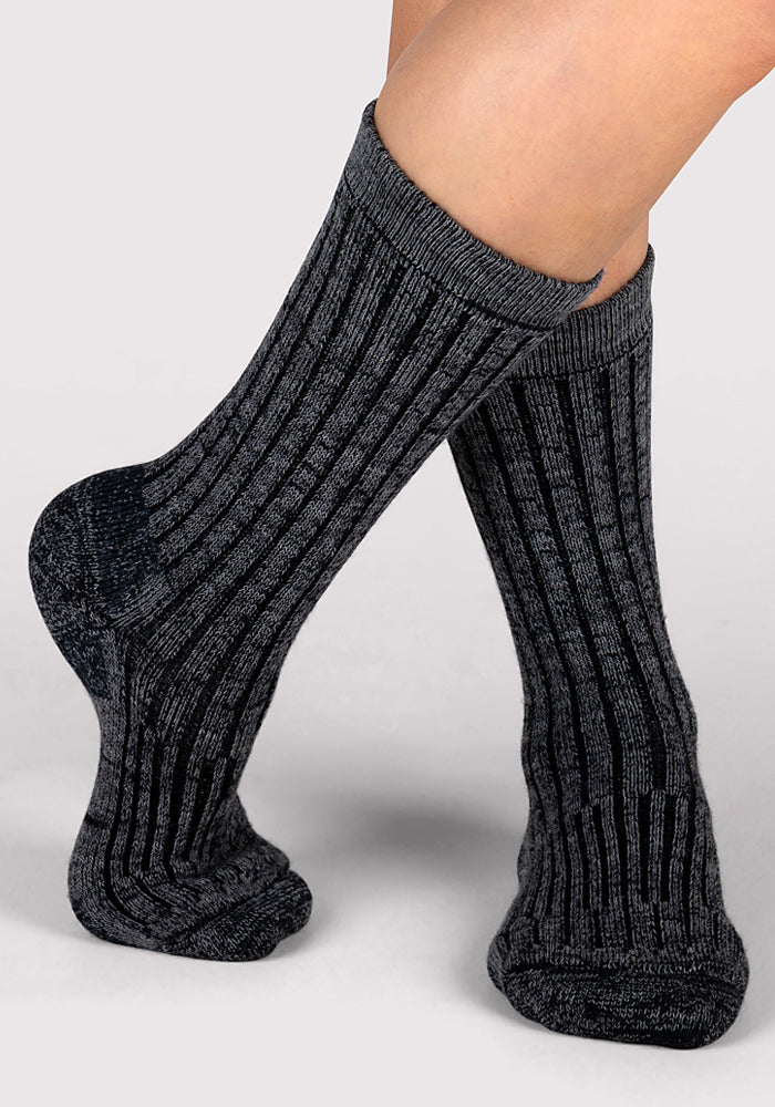 A close-up shows two feet wearing Woolx Womens Joey Crew Socks in Stone Grey with a subtle ribbed pattern, set against a plain light background.