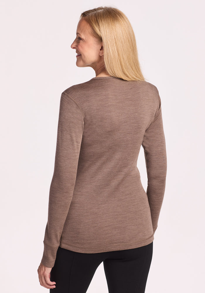 A woman with straight blonde hair faces away from the camera, wearing the Woolx Hannah Long Sleeve Top in Simply Taupe and black pants, set against a plain light background.