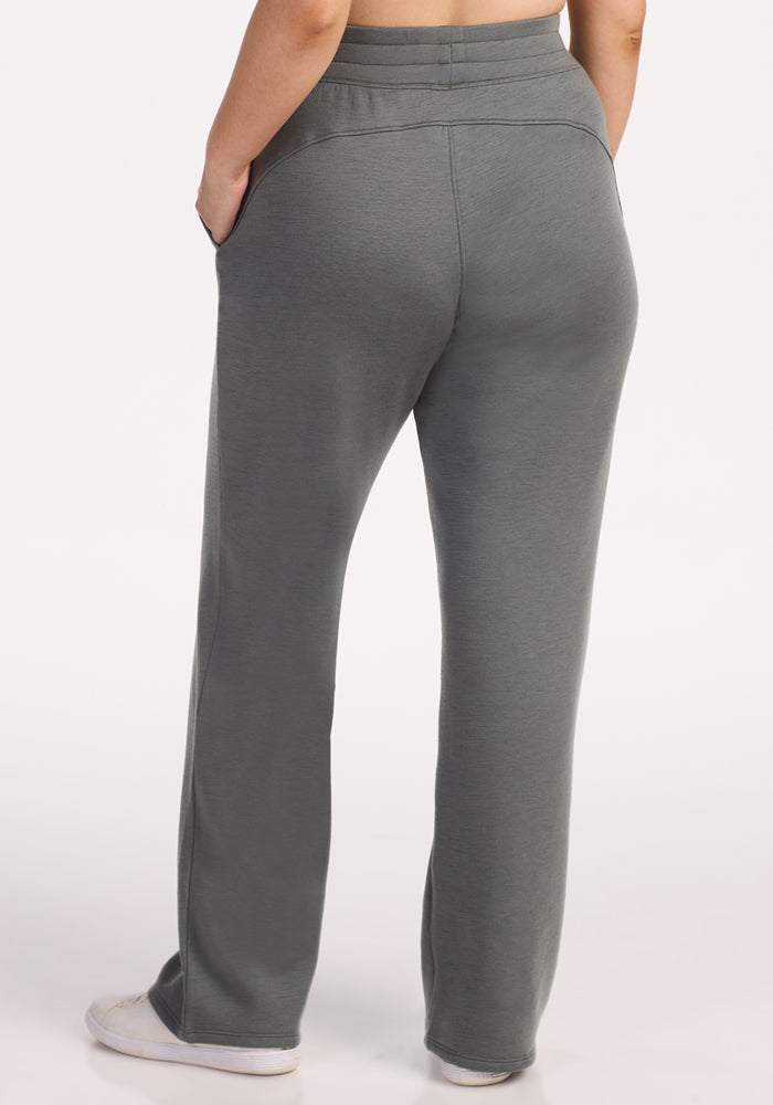 A person is shown from the back, hands in pockets, wearing Woolx Bree Lounge Pants in Sedona Sage with white sneakers, against a light background.