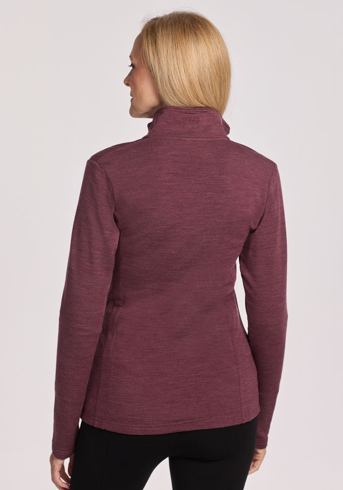 A woman with straight blonde hair is shown from the back, wearing the Woolx Finley Zip Up Sweatshirt in Grape Harvest Melange and black pants against a plain light background.
