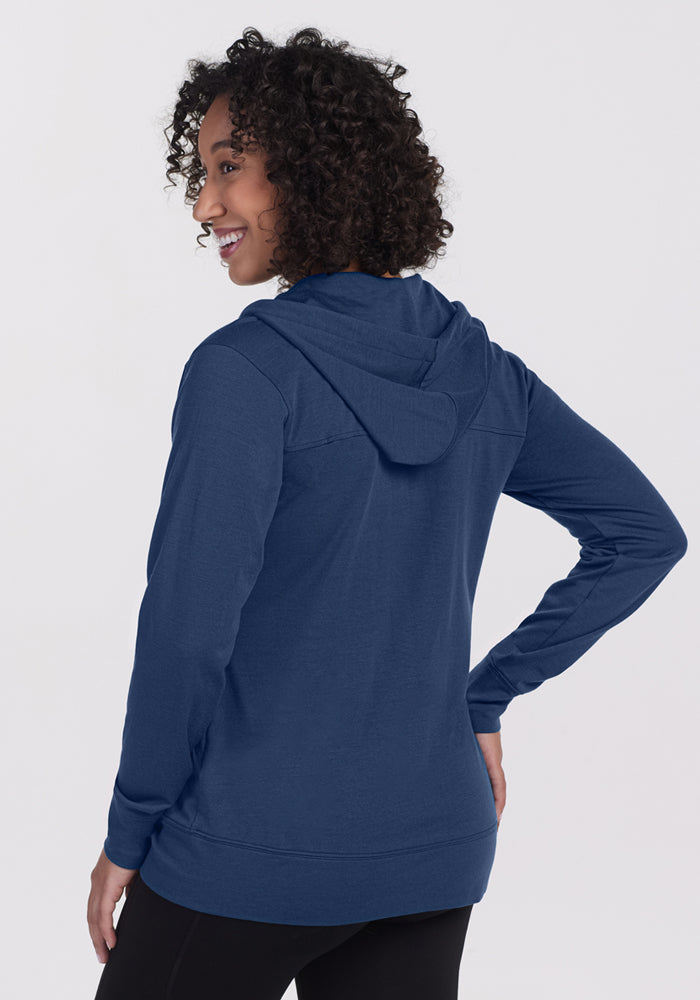 A person with curly hair models the Woolx Ryann Hoodie in Starry Night, facing away and smiling over their left shoulder against a plain, light background—capturing a travel-ready vibe.