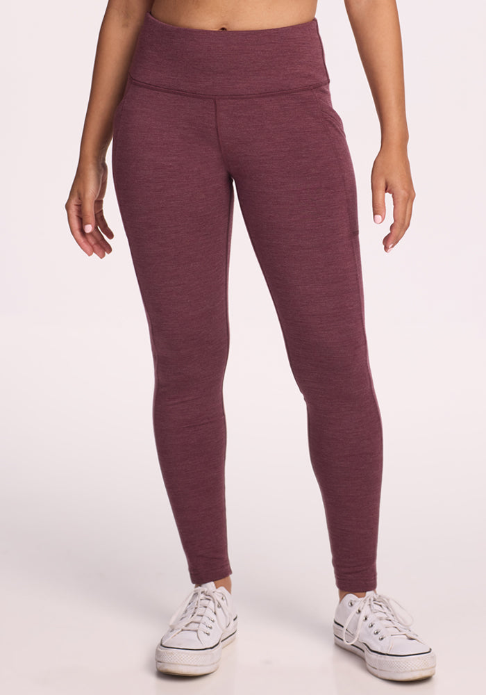 A person stands facing forward in Woolx Frost Duralite® Leggings - Grape Harvest Melange, with arms relaxed at their sides and wearing white sneakers, set against a plain light background. 