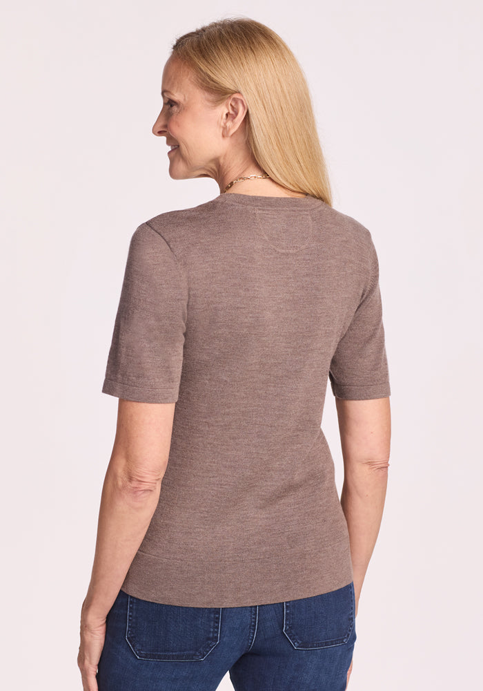 A woman with long blonde hair, slightly turned to the side, wears the Woolx Anna Crew Sweater in Simply Taupe and blue jeans against a light background.