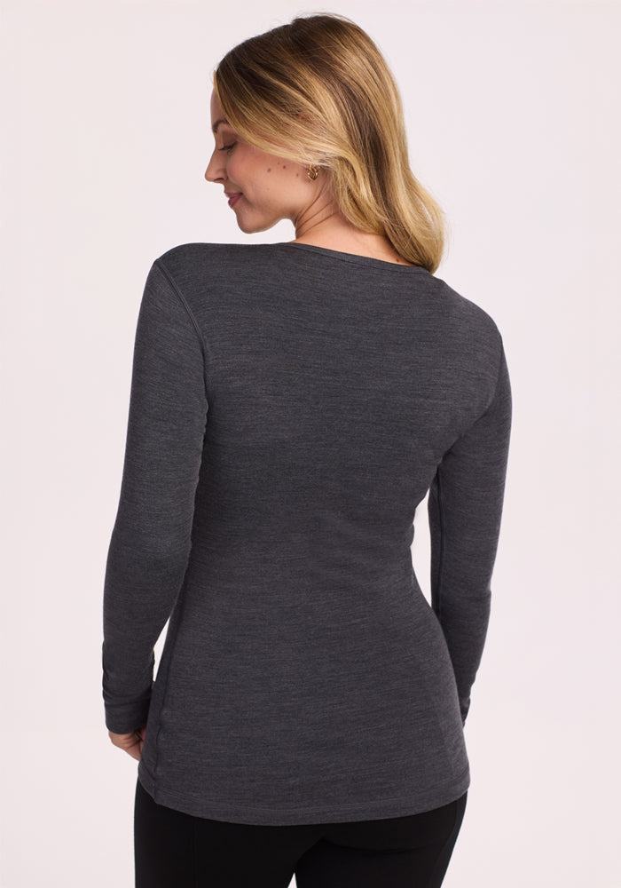 A woman with blonde hair models the Woolx Hannah Long Sleeve Top in Cinder Melange, standing with her back to the camera and looking over her left shoulder against a plain light background.