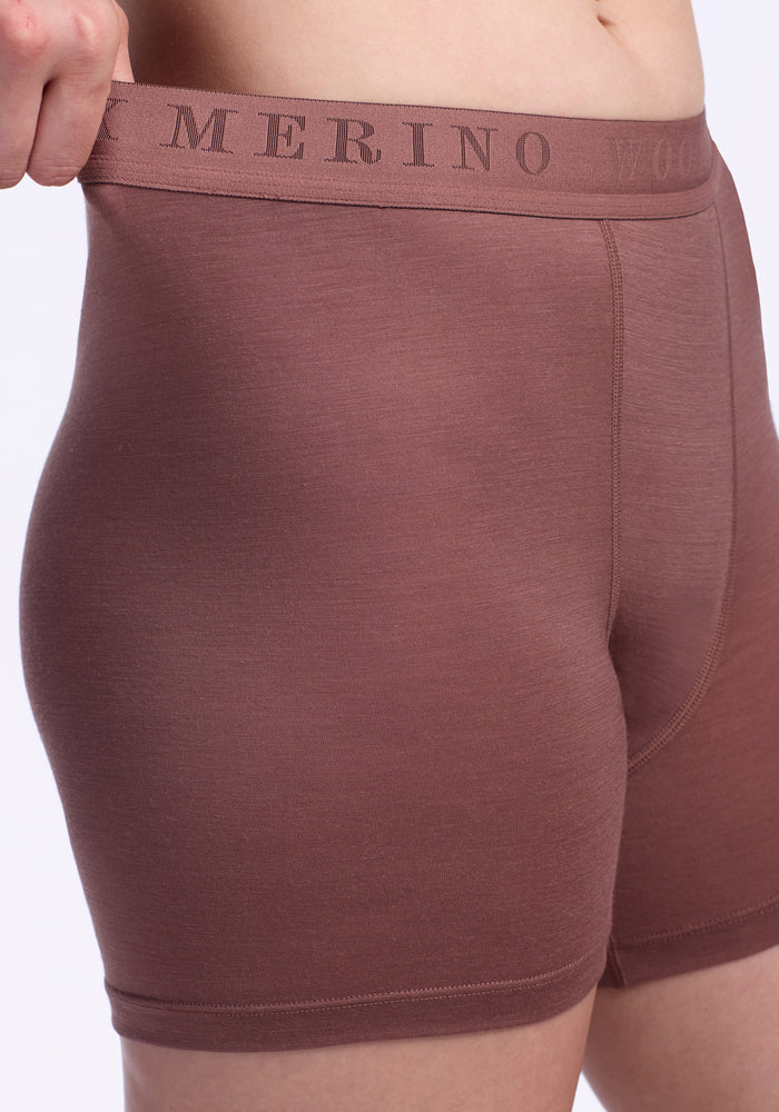 Close-up of a person wearing Woolx Elliott Boyshorts in Nutmeg, with one hand pulling the waistband which features "MERINO WOOL" printed on it.