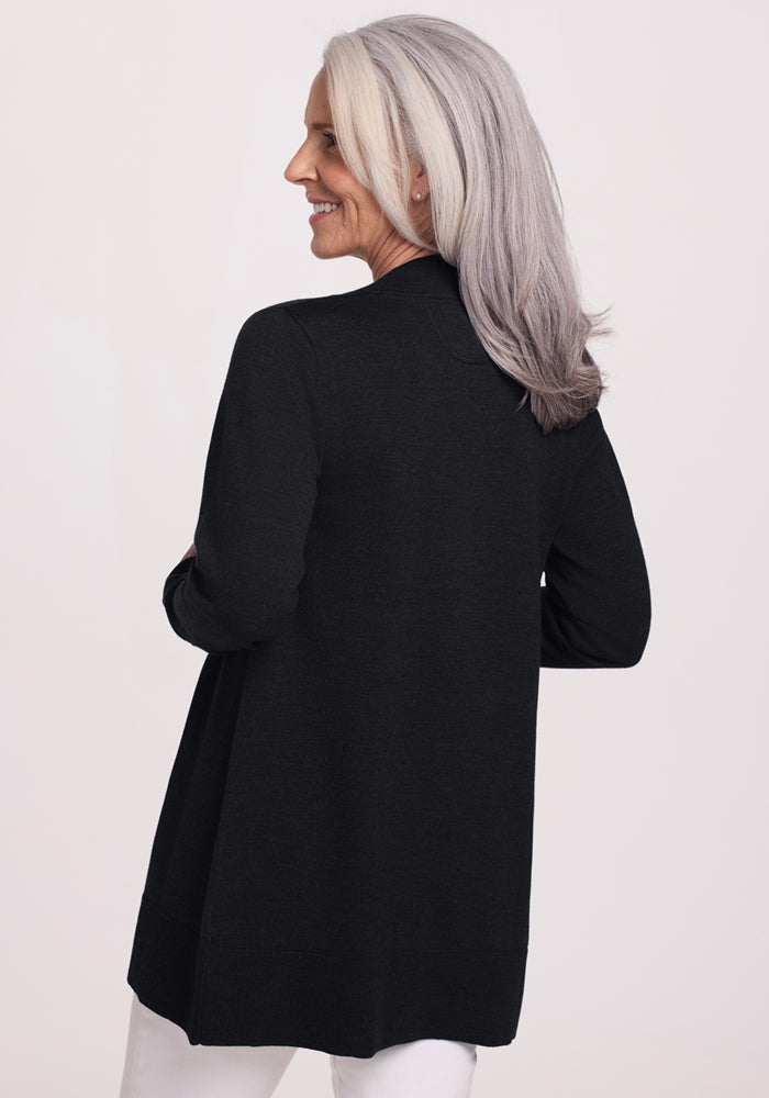 A woman with long gray hair smiles while standing and facing away, wearing the Woolx Macie Sweater in black and white pants against a light background.