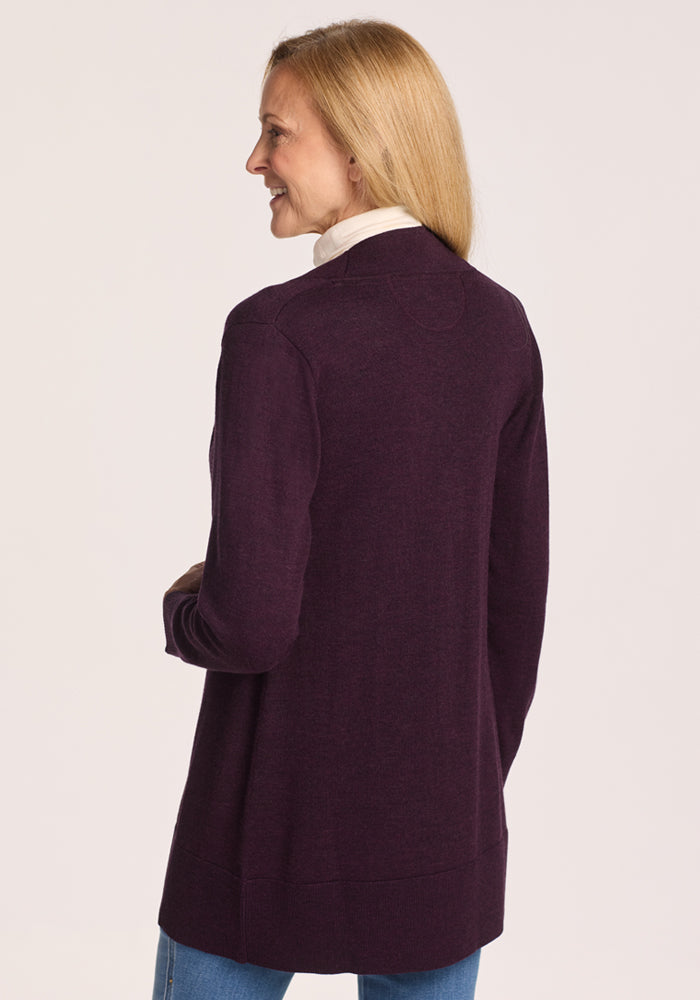 A woman with long blonde hair, smiling as she turns to the side, models the Woolx Macie Sweater in Deep Plum over a white turtleneck and light blue jeans.