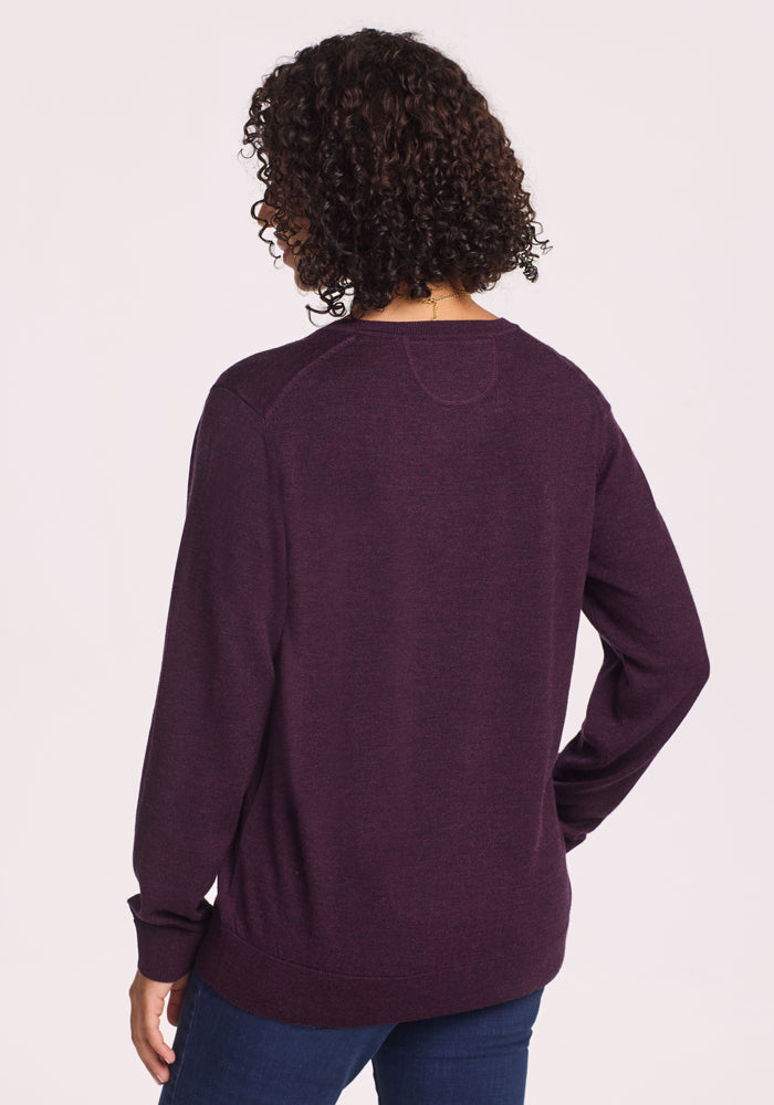 A person with curly hair, seen from behind, wears the Woolx Francesca Sweater in Deep Plum and blue jeans against a plain light background.