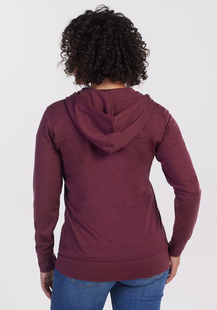 A person with curly hair is seen from behind in the Woolx Ryann Hoodie - Grape Harvest and blue jeans, standing against a plain white background.