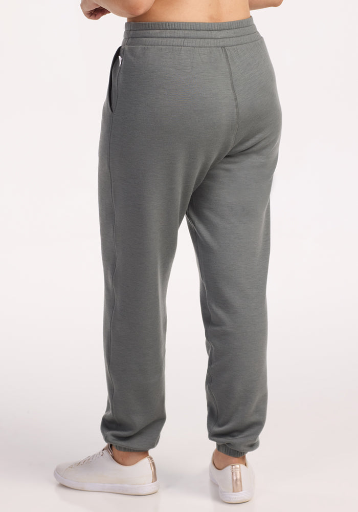 Someone wearing Woolx Parker Sweatpants in Sedona Sage and white sneakers stands on a white background, shown from the back with one hand in a pocket.