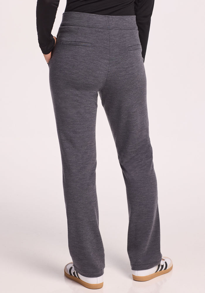 A person wearing Woolx Emerson Straight Leg Pants Petite in Cinder Melange and white sneakers with black stripes stands hands in pockets, facing away from the camera against a light background.