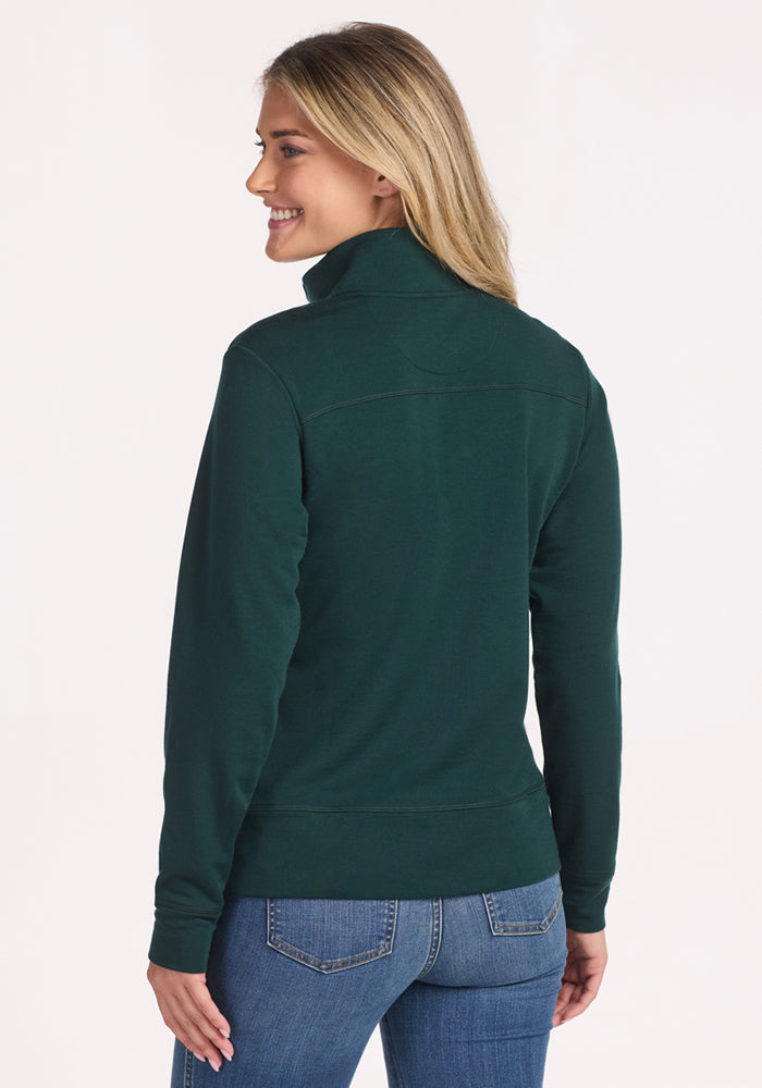 A woman with long blonde hair, smiling and facing away from the camera, wears the Woolx Annie 3 Button Pullover in Deep Timber and blue jeans against a plain light background.