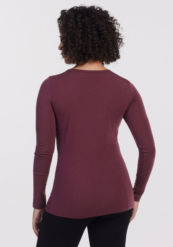 A person with curly hair wears the Woolx Layla V Neck Top in Grape Harvest and black pants, shown from behind against a plain white background.