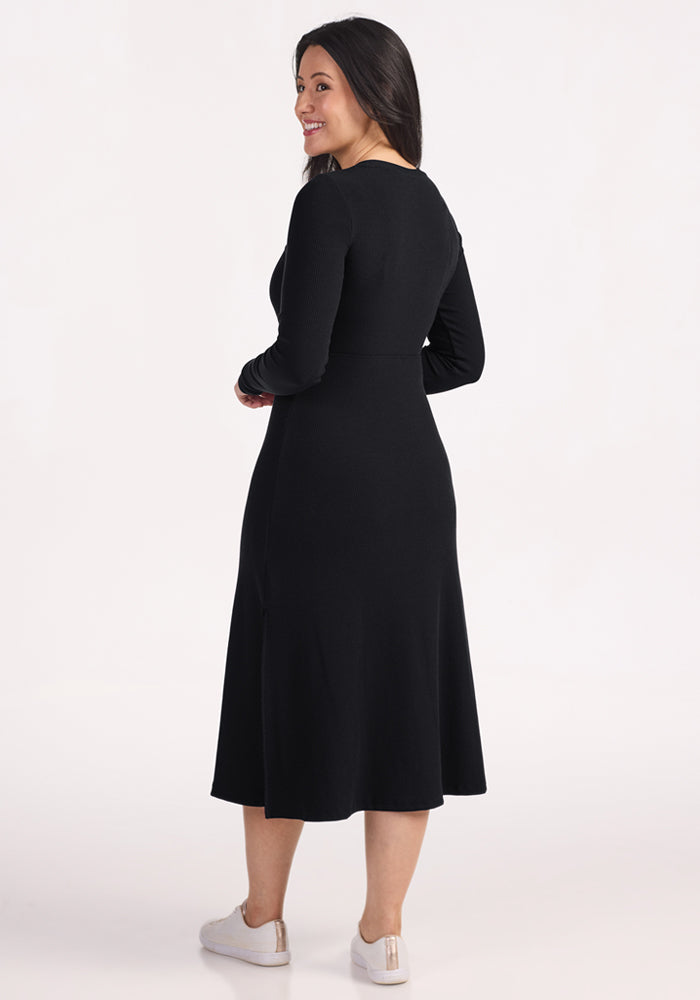 Woman in a Woolx Caroline Ribbed Twirl Dress - Black and white sneakers, smiling over her shoulder against light background.