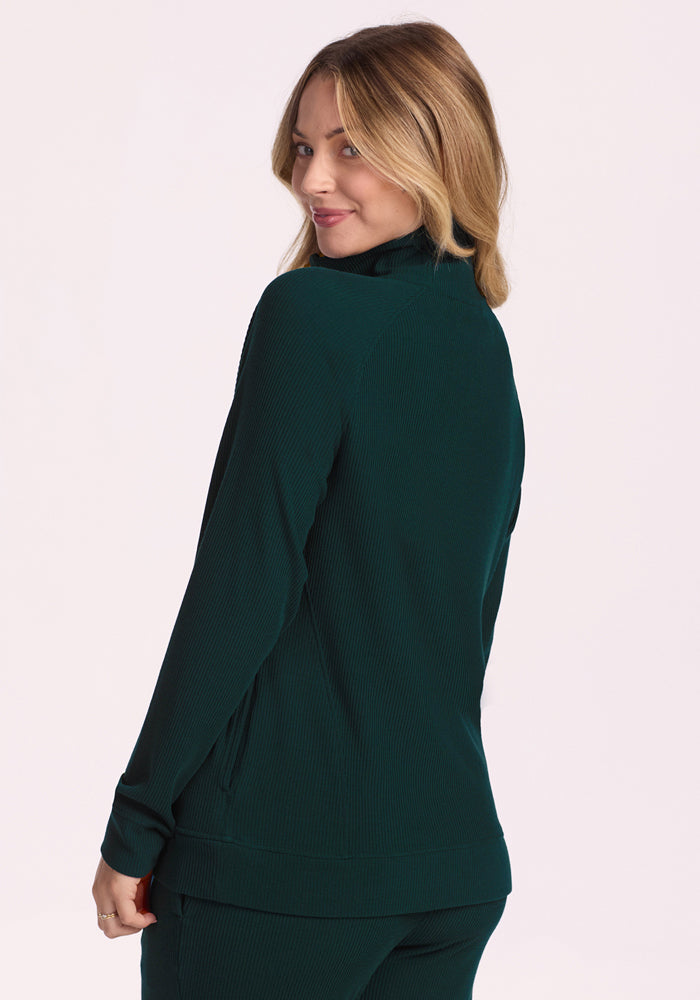 A woman with light brown hair wears the Woolx Quinn Ribbed 1/4 Zip in Deep Timber, standing slightly turned from the camera and smiling over her shoulder against a plain light background.