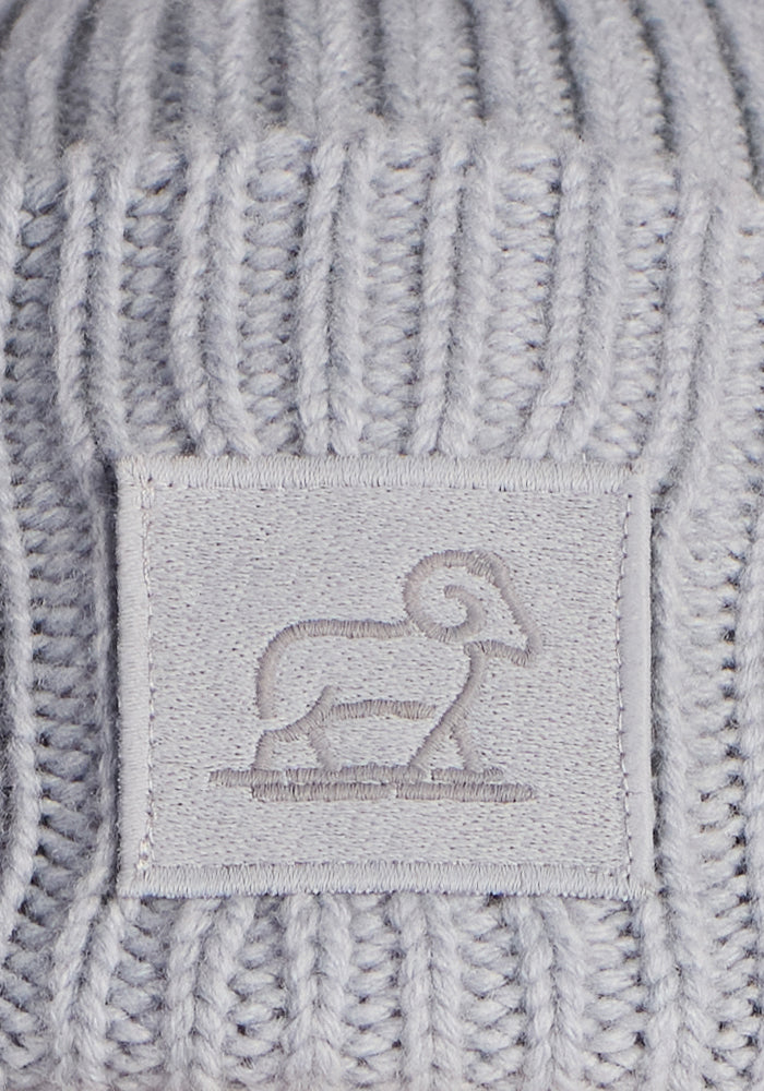 The Woolx Ria Chunky Beanie in Morning Fog is a light gray ribbed knit merino wool hat featuring a rectangular patch with an embroidered ram outline—ideal for cozy winter wear.