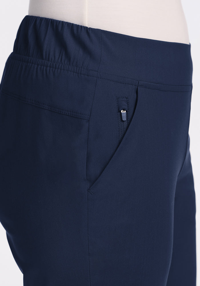 Close-up side view of a person wearing Woolx Nicole Ankle Pants in Deep Navy, featuring an elastic waistband, zippered pocket, and a tapered-leg fit.