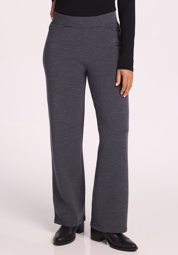 A person wearing Woolx Ellie Wide Leg Pants Petite in Cinder Melange, a black long-sleeve top, and black boots stands against a light background. Only the lower half of their body is visible.