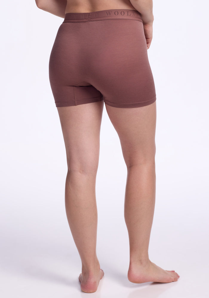 A person stands barefoot, facing away from the camera, wearing Woolx Elliott Boyshorts in Nutmeg, temperature-regulating underwear shorts, against a plain white background.