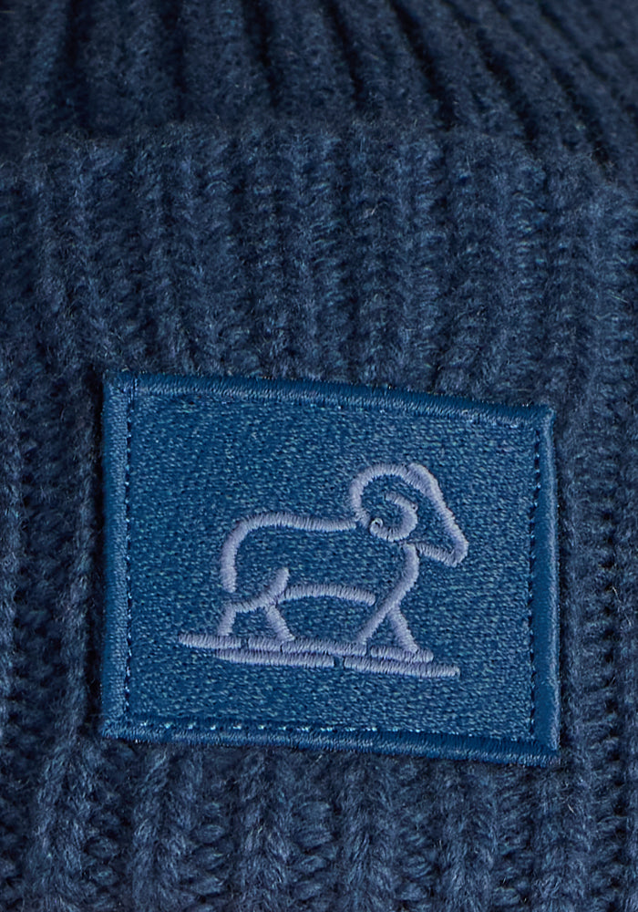 A close-up of the Woolx Ria Chunky Beanie in Starry Night, showing its blue merino wool knit and a matching rectangular patch with an embroidered sheep outline—a cozy and stylish winter accessory.