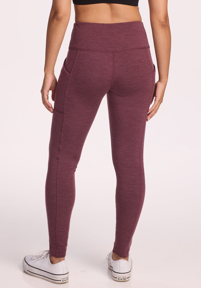 A person is shown from the back against a plain light background, wearing Woolx Frost Duralite® Leggings in Grape Harvest Melange featuring a high-waisted fit, side pockets, and paired with white sneakers.