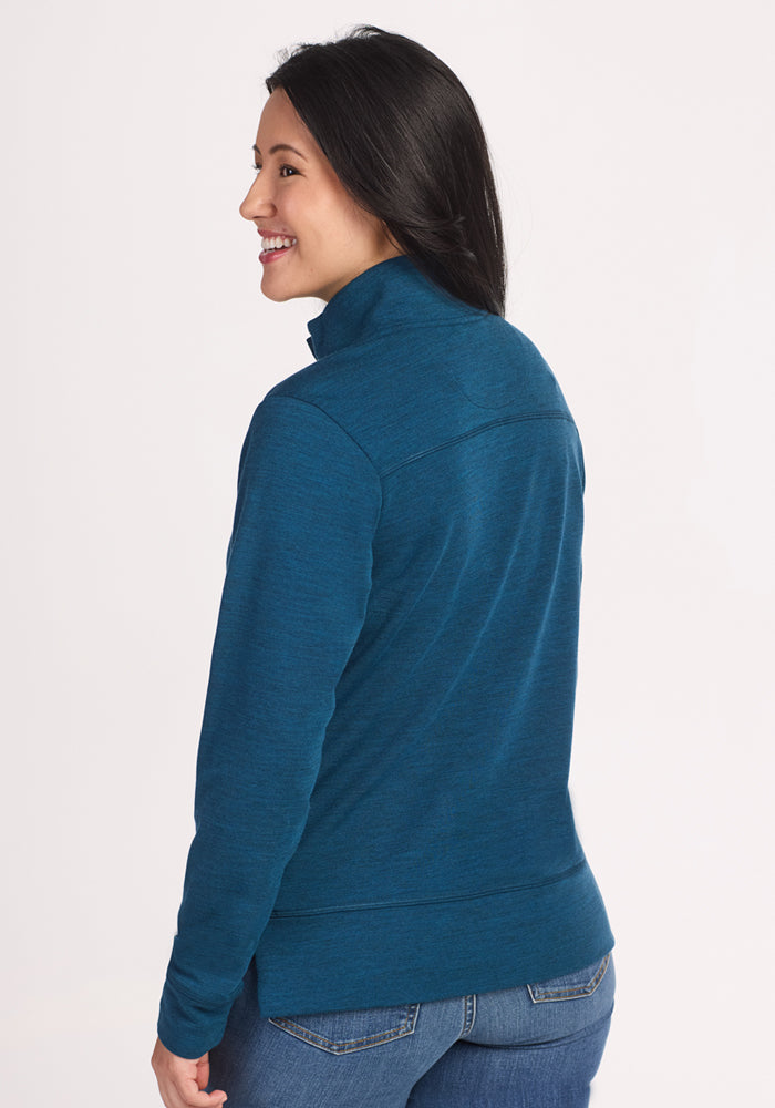 A woman with long dark hair smiles, looking to the side while wearing the Woolx Annie 3 Button Pullover in Majolica Blue and jeans, against a plain light background.