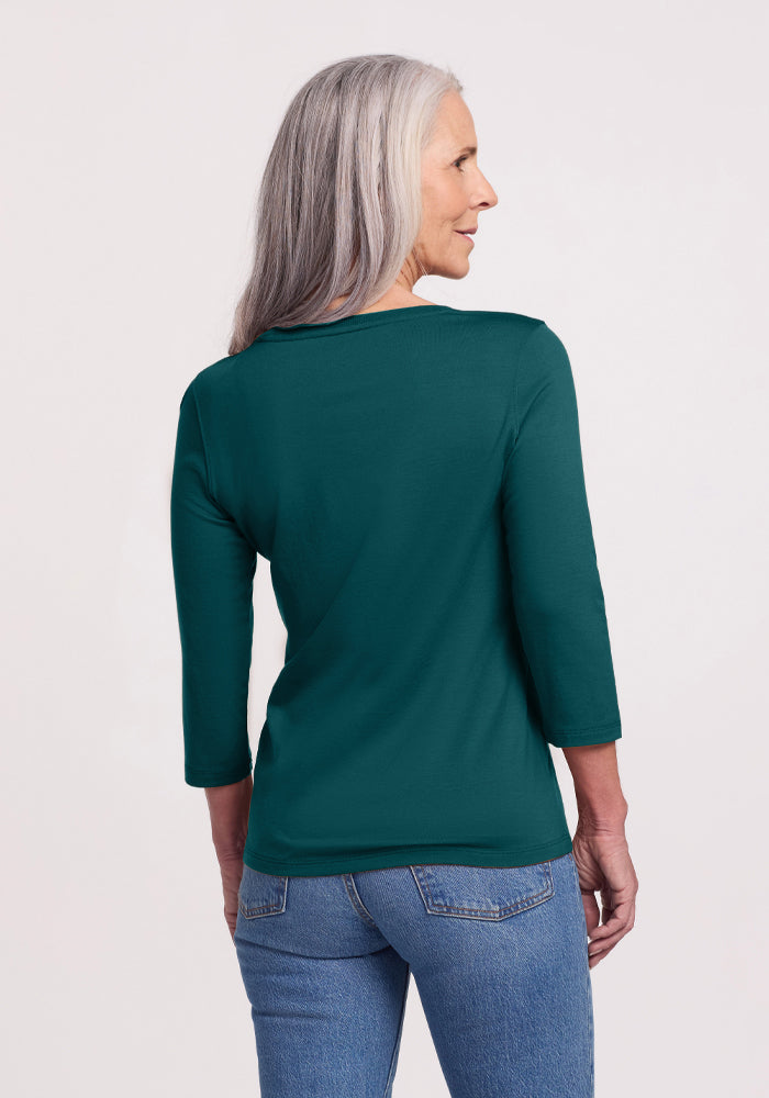 A woman with long gray hair, seen from behind, wears the Woolx Jenny 3/4 Sleeve Crew Neck in Riverbank Green and blue jeans against a light background.