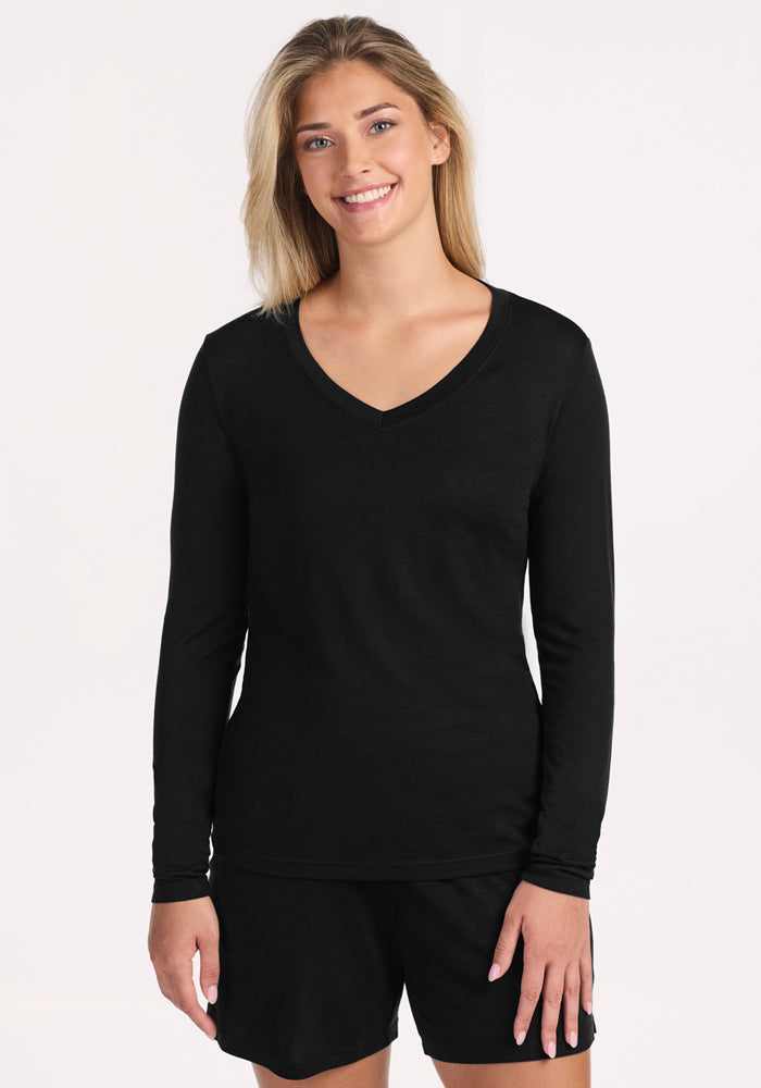 A smiling blonde woman stands against a plain light background, wearing the Woolx Lily V Neck Lounge Top in black—ideal travel sleepwear for anyone dealing with night sweats. 