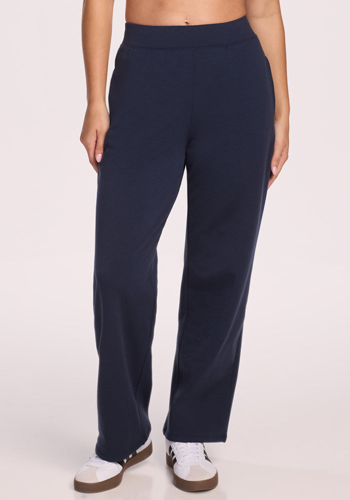 A person wearing Woolx Brynn Pants in Deep Navy and white sneakers with black accents stands against a plain light background.