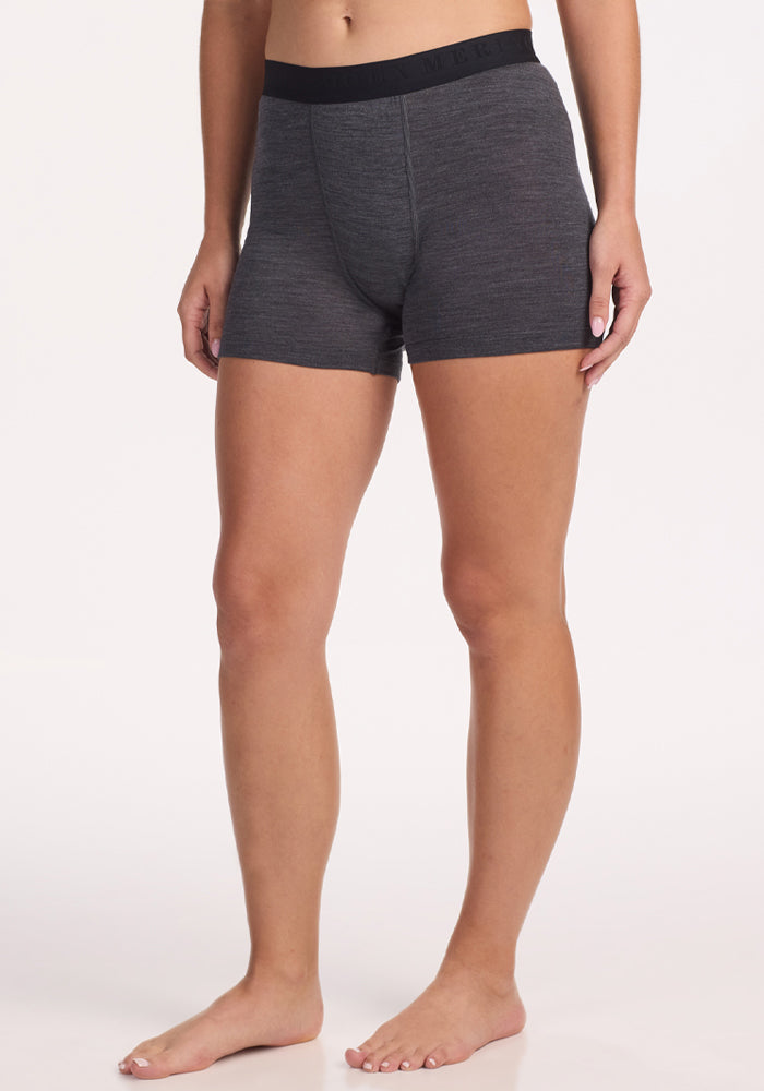 A person stands barefoot, wearing Woolx Elliott Boyshort in Cinder Melange with a black waistband, shown from mid-torso to feet against a plain white background. 