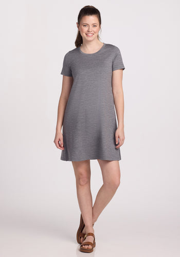 A person wearing the Woolx Georgie Dress in Graphite Heather and brown sandals smiles against a white background, arms relaxed by their sides. | Lilly is 5’9”, wearing a size S