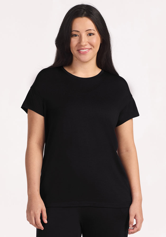 A woman with long dark hair smiles against a light background, wearing the Woolx Billie Lounge Tee in black and matching pants—ideal for stylish lounging or restful nights. 