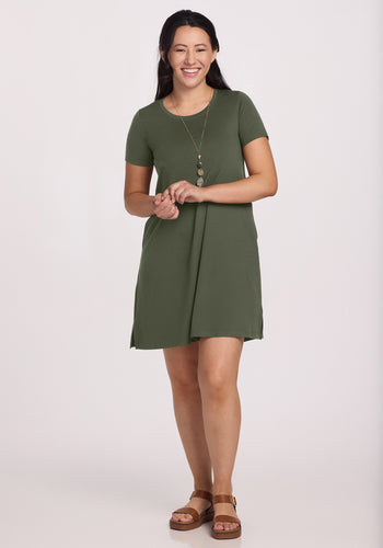 A woman smiles wearing the Woolx Georgie Dress in Green Meadow, accessorized with a long necklace and brown sandals, against a plain light background. | Sarah is 5'8", wearing a size S