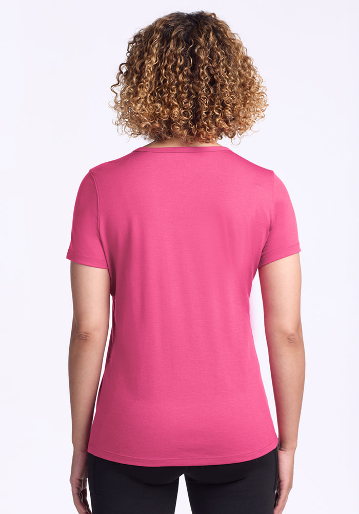 A person with curly hair is shown from the back, wearing the Woolx Liza Crew Neck Tee in Raspberry Fizz and black pants against a plain white background.