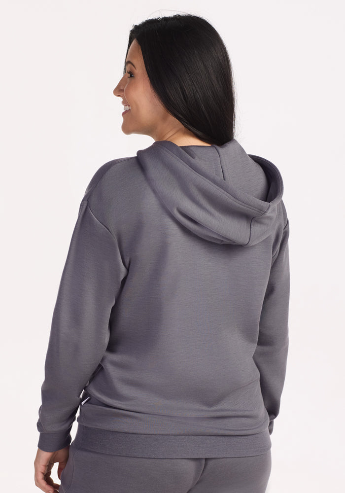 A woman with long dark hair smiles while wearing the Woolx Avery Hoodie in Arctic Dusk, shown from the back against a plain light background.