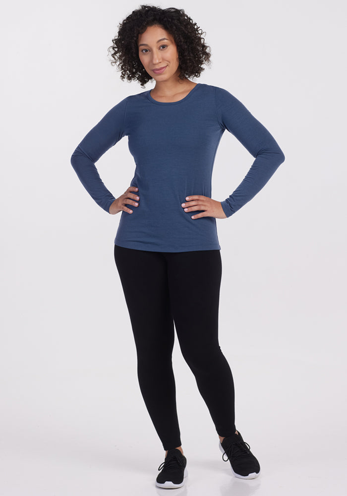 A woman with curly hair stands confidently, wearing the Woolx Remi Long Sleeve T Shirt in Starry Night, paired with black leggings and sneakers, against a plain white background.