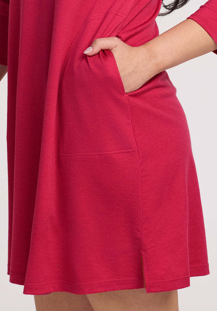 Someone models the Woolx Rissa A Line Dress in Poppy Spark, with their right hand in the side pocket to highlight its convenience and side slit—ideal for layering during fall and winter.