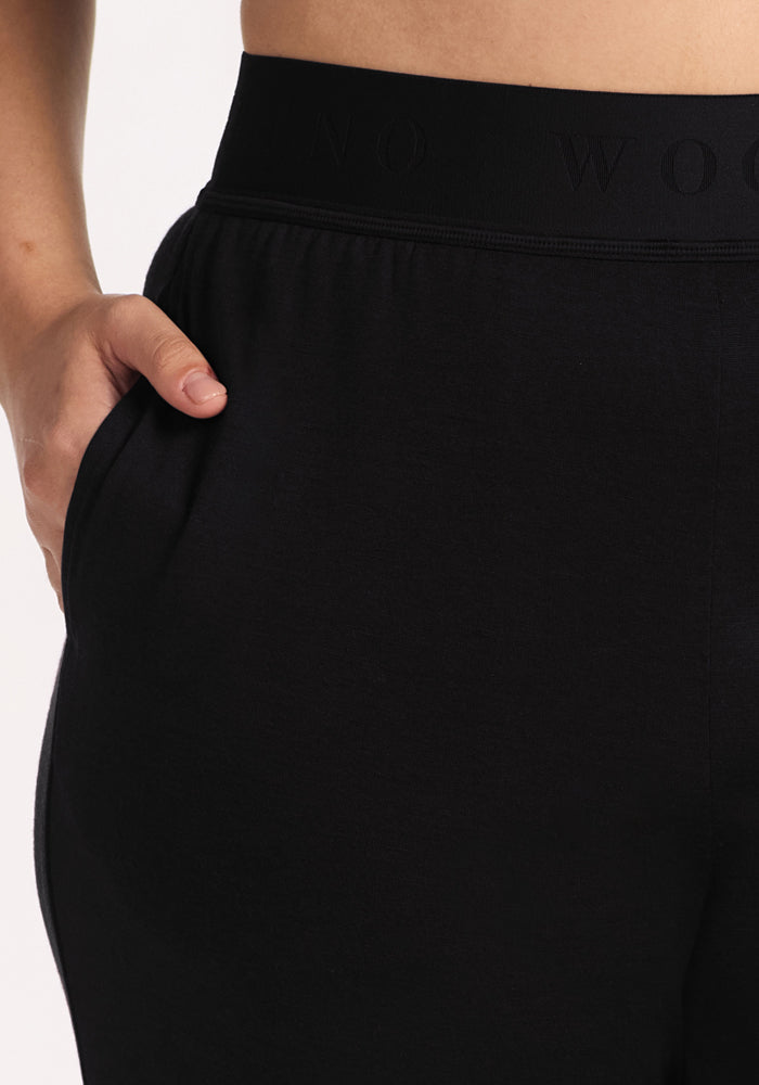 A close-up of a person wearing Woolx Maya Lounge Pants - Black, with one hand in the pocket, highlighting the wide leg design, waistband, and hip.