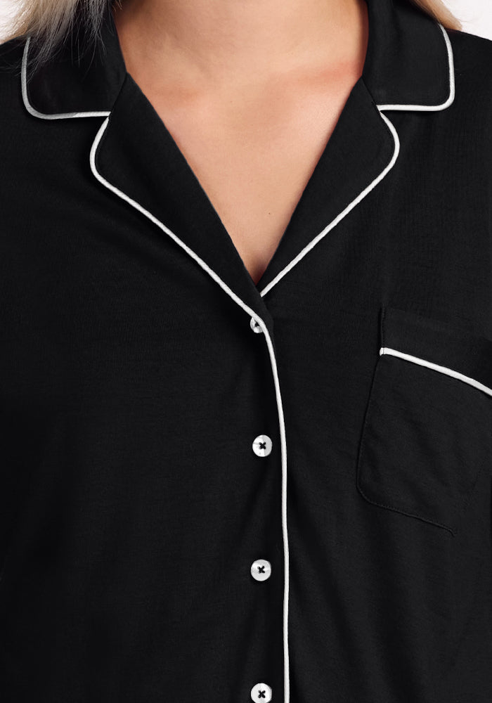 Close-up of a person wearing the Woolx Harper FeatherTouch® Pajama Set in Black, featuring white piping on the collar, button placket, and pocket. The top has white buttons and a visible chest pocket; face not shown.
