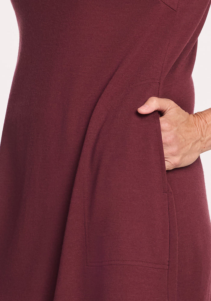 A close-up of a person wearing the Woolx Cassie Dress in Toasted Garnet, one hand in a side pocket, highlighting the travel-friendly pocket detail.