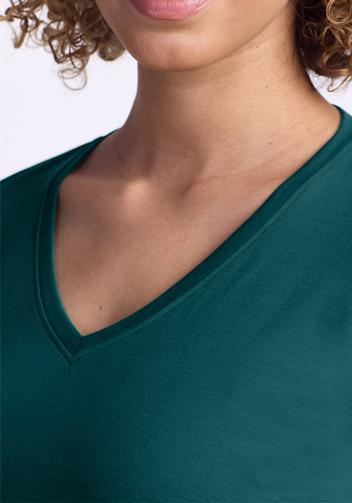 Close-up of a person wearing the Woolx Millie Long Sleeve in Riverbank Green. The shot focuses on their lower face, neck, and upper chest, with curly light brown hair visible. This top offers temperature regulation for comfort and style.