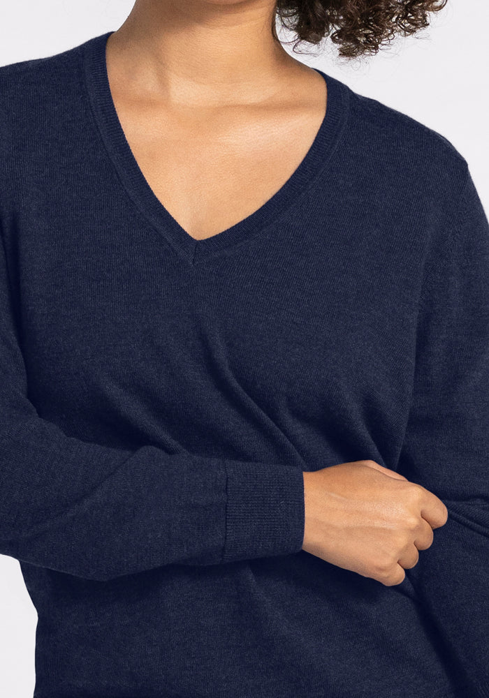 A person wearing the Woolx Francesca Sweater in Storm Cloud, a long-sleeve Merino wool top, stands with one arm folded across their body. Their head is partially out of frame against a plain light gray background.
