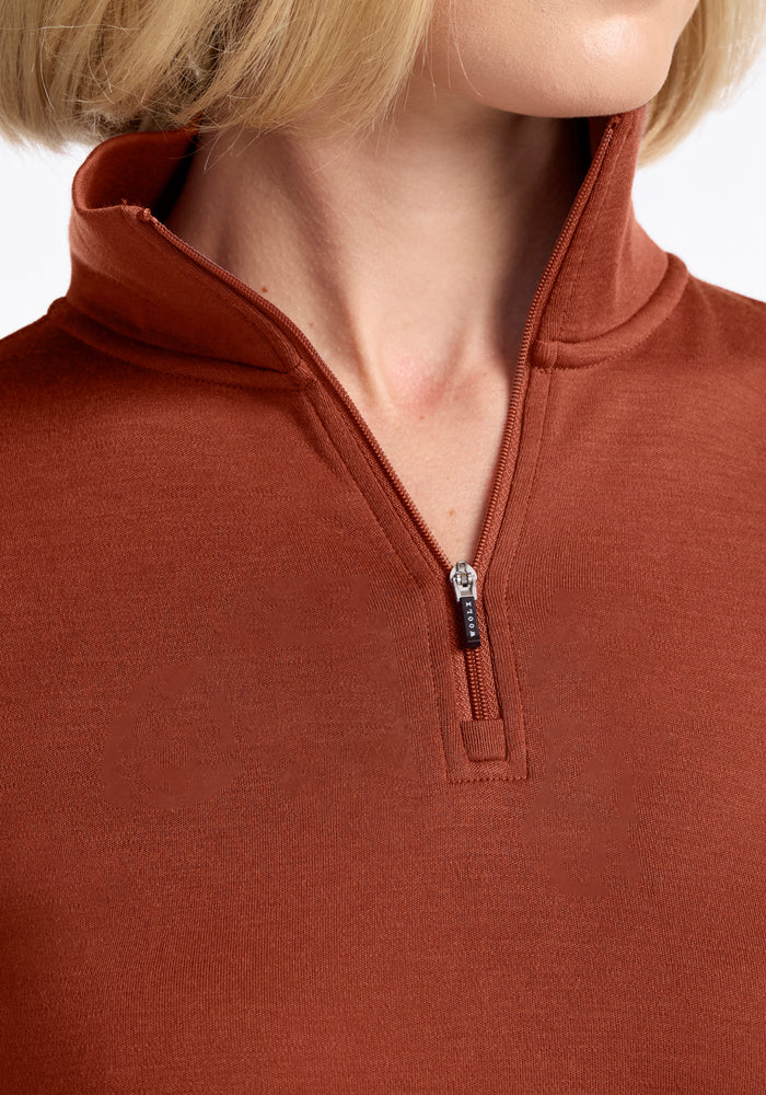 A close-up of a person with short blonde hair and light skin wearing the Woolx Brooke 1/4 Zip in Maple Leaf, with the collar standing up and the zipper partially open.
