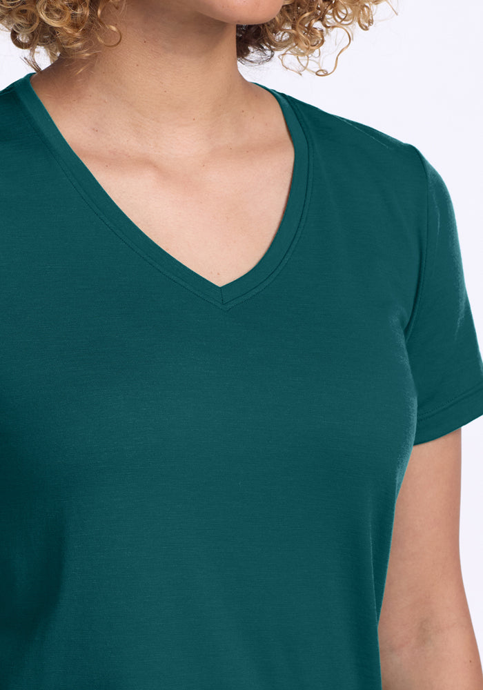 A person with light skin and curly hair wears the Woolx Junie V Neck in Riverbank Green. The image, cropped at the shoulders and chin, highlights the shirt’s soft neckline and relaxed, comfortable style.