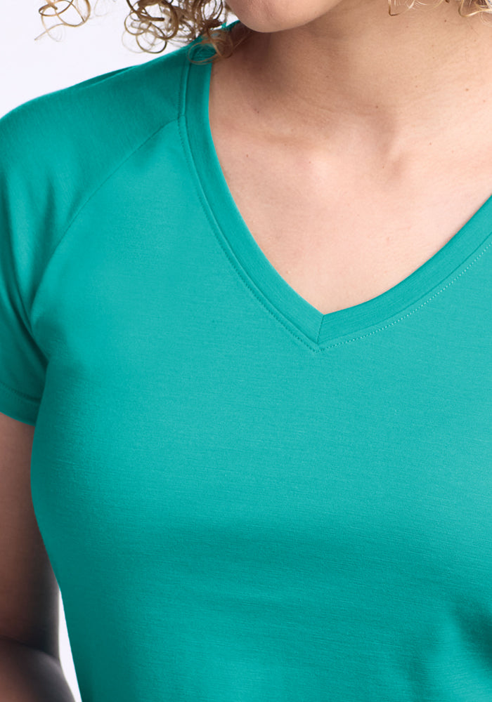 Close-up of Woolx Mia V Neck - Cool Jade. Moisture-wicking fabric and the flattering neckline are shown, with a partial view of curly hair and chin, focusing on the shirt's teal color, texture, and fit.