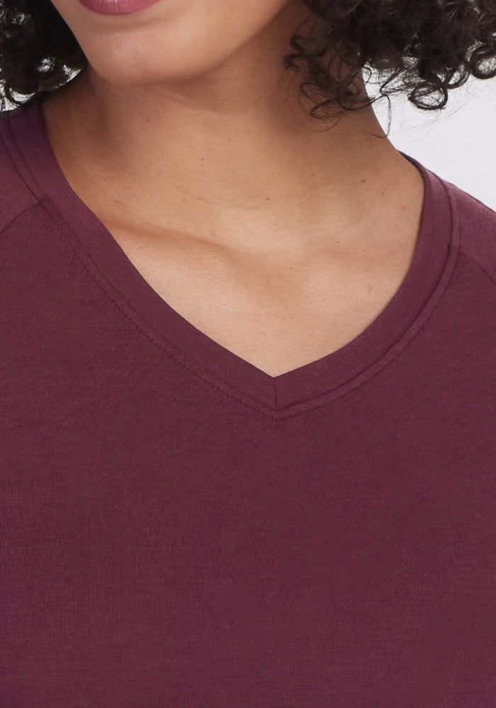 A close-up of a person wearing the Woolx Mia V Neck in Grape Harvest, highlighting the V-neckline, part of the chest and chin, with some curly hair visible.