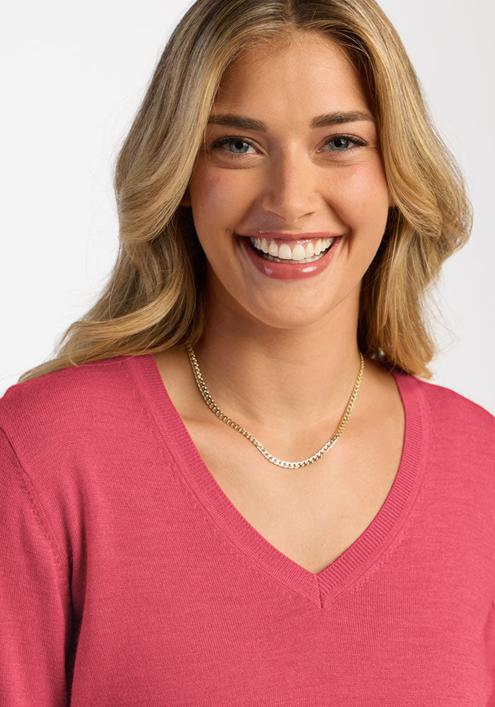 A smiling woman wears a fuchsia Francesca Sweater - Vivid Rose merino wool V-neck and a gold chain necklace.