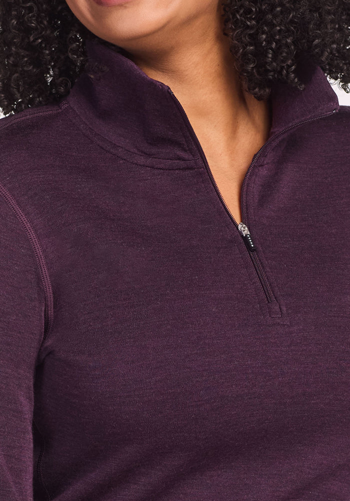 A person with curly hair models the Woolx Brooke 1/4 Zip in Deep Plum, partially unzipped at the collar, against a plain background.