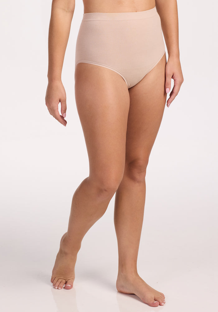 A person stands barefoot on a white background, wearing Woolx Mabel Full Coverage Underwear in Sand. Their arms are relaxed at their sides and their face is not visible, emphasizing the seamless comfort of these high-waisted merino wool undies.